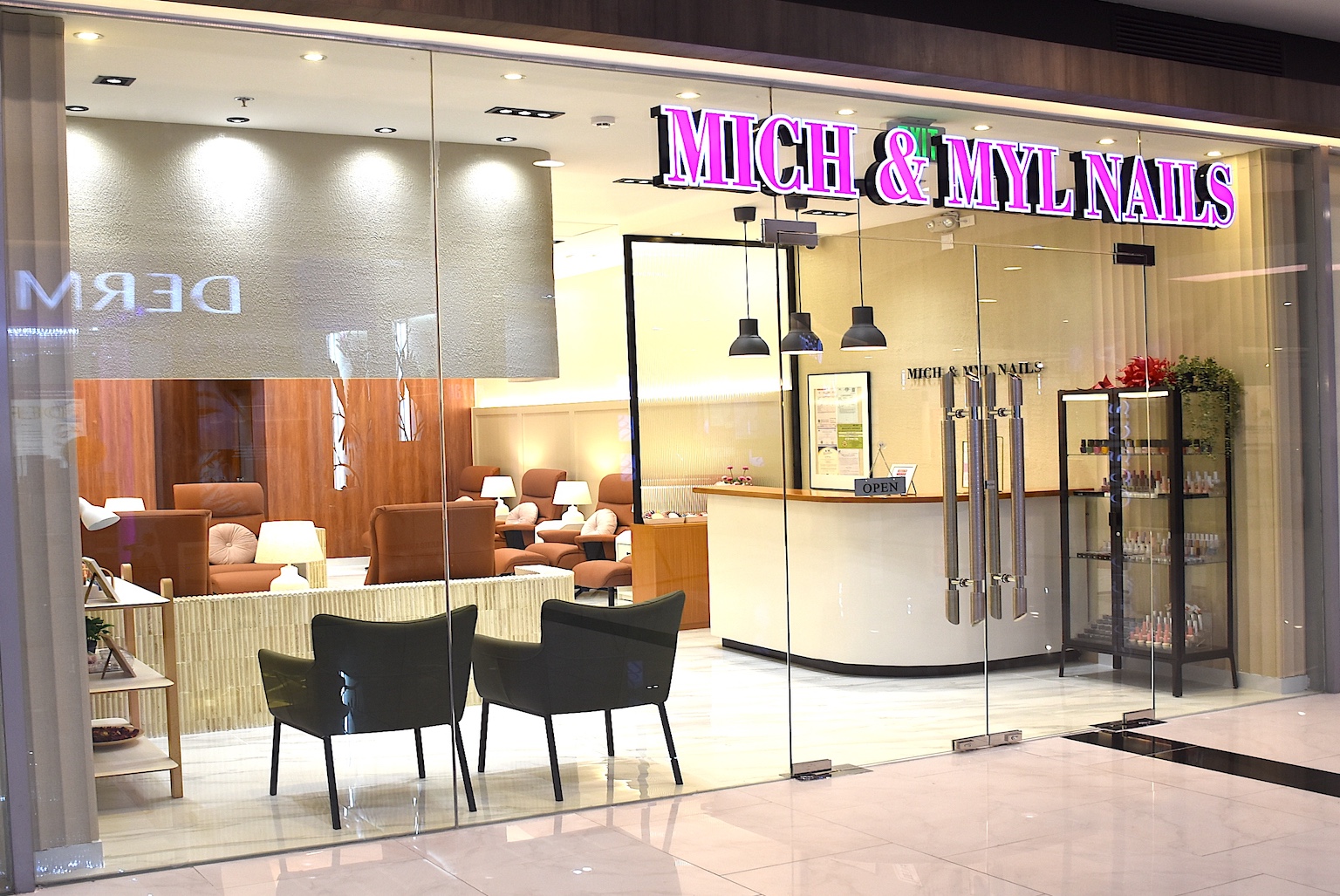 Exterior view of a bright nail salon with a glass storefront labeled 'MICH & MY-NAILS' and a reception desk inside.