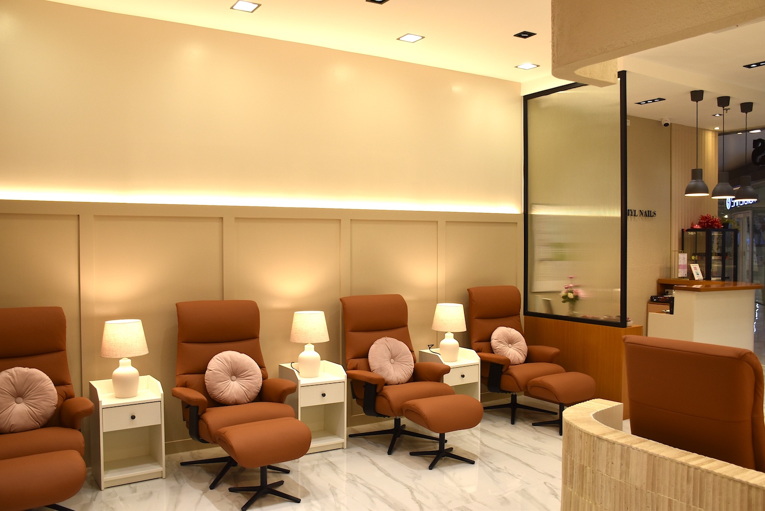 Row of brown leather recliners with round pink cushions, white side tables, and lamps in a spa waiting area.