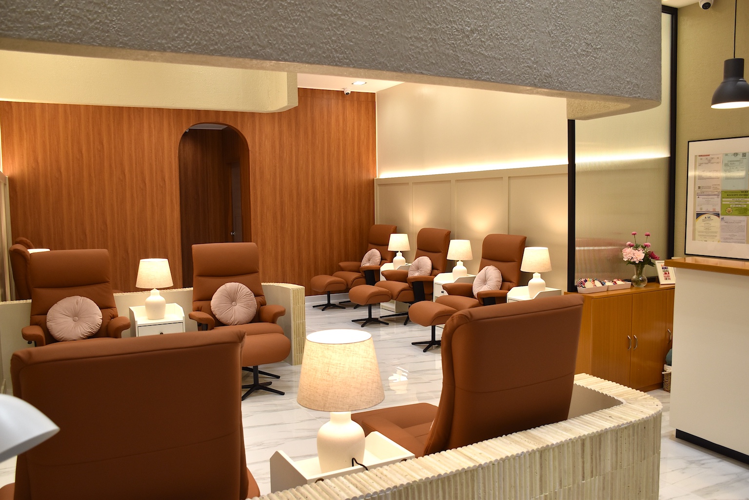Brown leather recliners and small lamps line a modern waiting room with wood paneling and a marble floor.